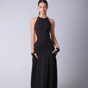 May include: A woman wearing a black maxi dress with a high neckline and cutouts on the sides. The dress has a flowing, relaxed fit. She is wearing black sandals.