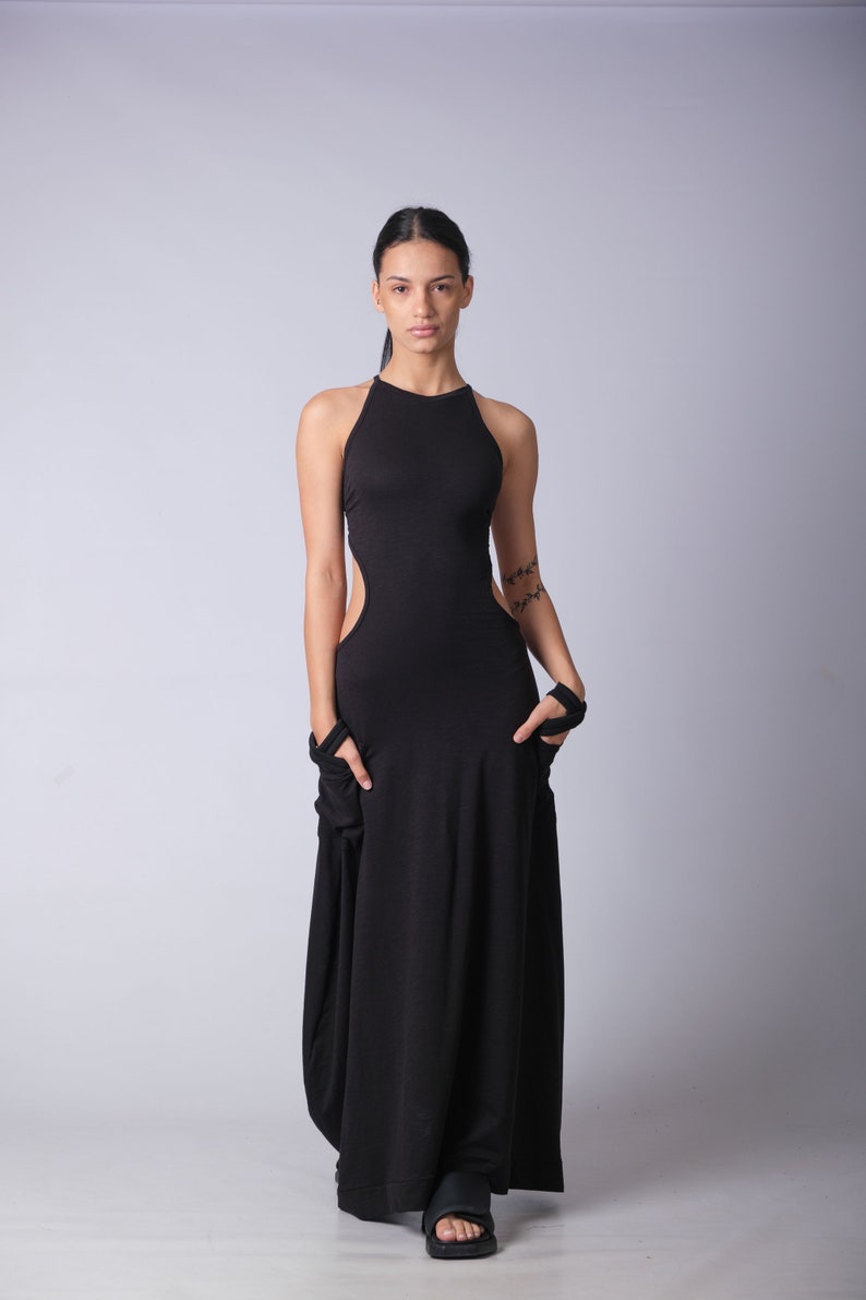 May include: A woman wearing a black maxi dress with a high neckline and cutouts on the sides. The dress has a flowing, relaxed fit. She is wearing black sandals.