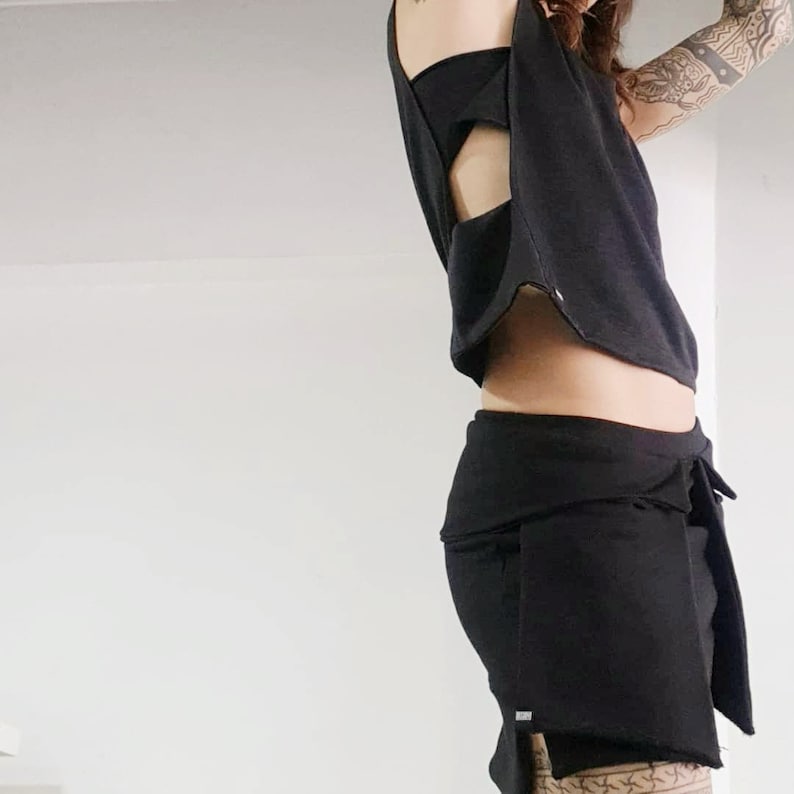 May include: A black crop top with a cut-out design in the back, paired with a black wrap skirt. The skirt has a long, flowing design and a tie at the waist.