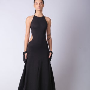 May include: A woman wearing a black maxi dress with a cut-out detail on the side. The dress has a halter neckline and a flowing skirt.