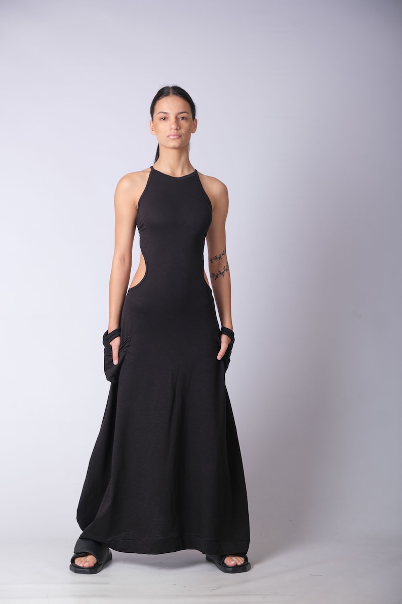 May include: A woman wearing a black maxi dress with a cut-out detail on the side. The dress has a halter neckline and a flowing skirt.