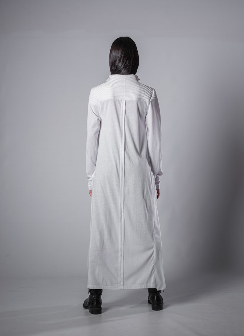 May include: A white long-sleeved maxi dress with a high neckline and a center seam down the back. The dress has a relaxed fit and a slightly flared skirt.