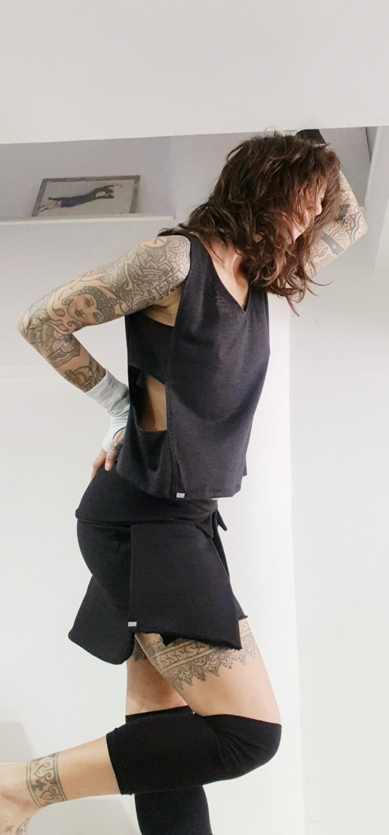 May include: A woman wearing a black sleeveless top and a black skirt. She has tattoos on her arms and legs.