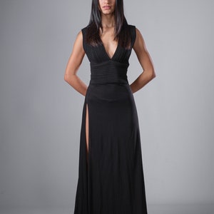 May include: A woman wearing a long black sleeveless dress with a plunging neckline and a high slit on the left side.
