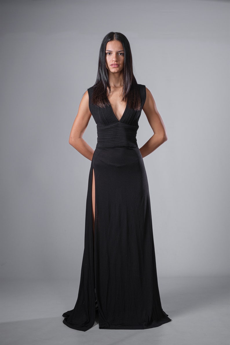 May include: A woman wearing a long black sleeveless dress with a plunging neckline and a high slit on the left side.