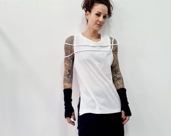 May include: A white sleeveless top featuring two horizontal straps across the chest and shoulders, paired with black fingerless gloves and black trousers. The top has a round neckline and a straight hemline, creating a clean and structured appearance.