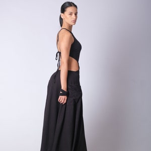May include: A woman wearing a black maxi dress with a cut-out design and a halter neckline. The dress has a flowing skirt and is made of a soft, comfortable fabric.