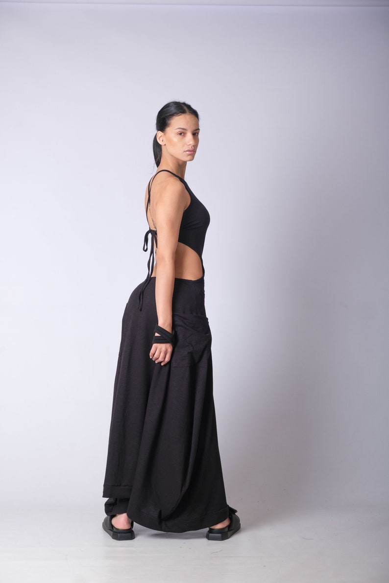 May include: A woman wearing a black maxi dress with a cut-out design and a halter neckline. The dress has a flowing skirt and is made of a soft, comfortable fabric.