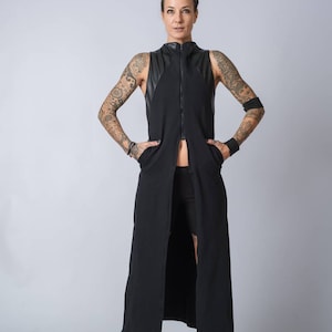 Puede incluir: Un vestido maxi negro sin mangas con una cremallera en la parte delantera y detalles de cuero. El vestido lo lleva una persona con tatuajes en los brazos.