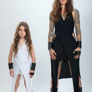 May include: Two people wearing long, white and black dresses with side slits. The dresses are similar in style and have a wrap-around design. Both people are wearing black bracelets and black shoes.