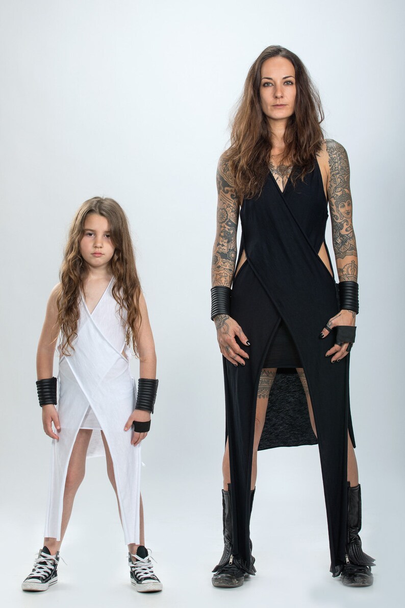 May include: Two people wearing long, white and black dresses with side slits. The dresses are similar in style and have a wrap-around design. Both people are wearing black bracelets and black shoes.