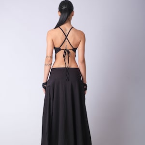 May include: A black, sleeveless top with a criss-cross back tie and a matching black maxi skirt. The skirt has a loose, flowing fit and a unique asymmetrical hemline.