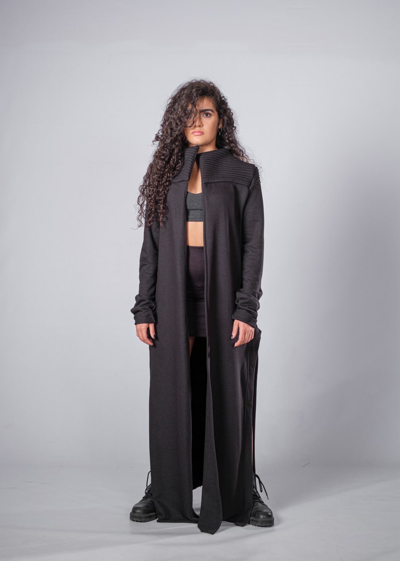 May include: A long black cardigan with a high collar and long sleeves. The cardigan is open in the front and has a long, flowing design.