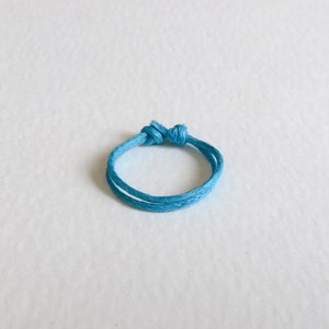 May include: A simple blue string tied into a circle, forming a ring.