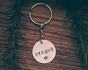 May include: Silver keychain with a round charm that says "STRONG" with a small heart symbol.