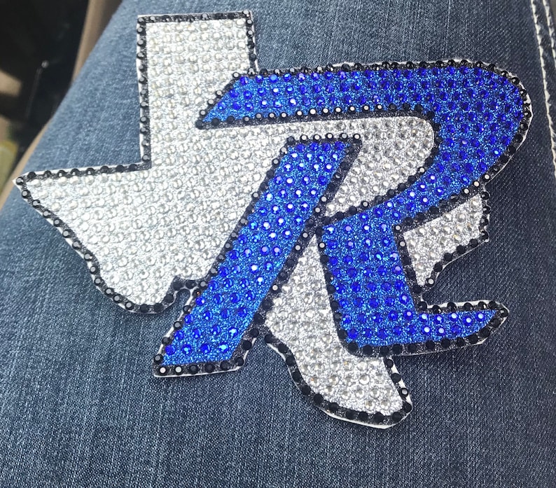 May include: A blue and white rhinestone patch in the shape of the state of Texas with the letter "R" in the center.
