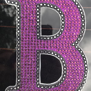 May include: A large, purple letter B made of rhinestones. The letter is outlined in black and has a white border.
