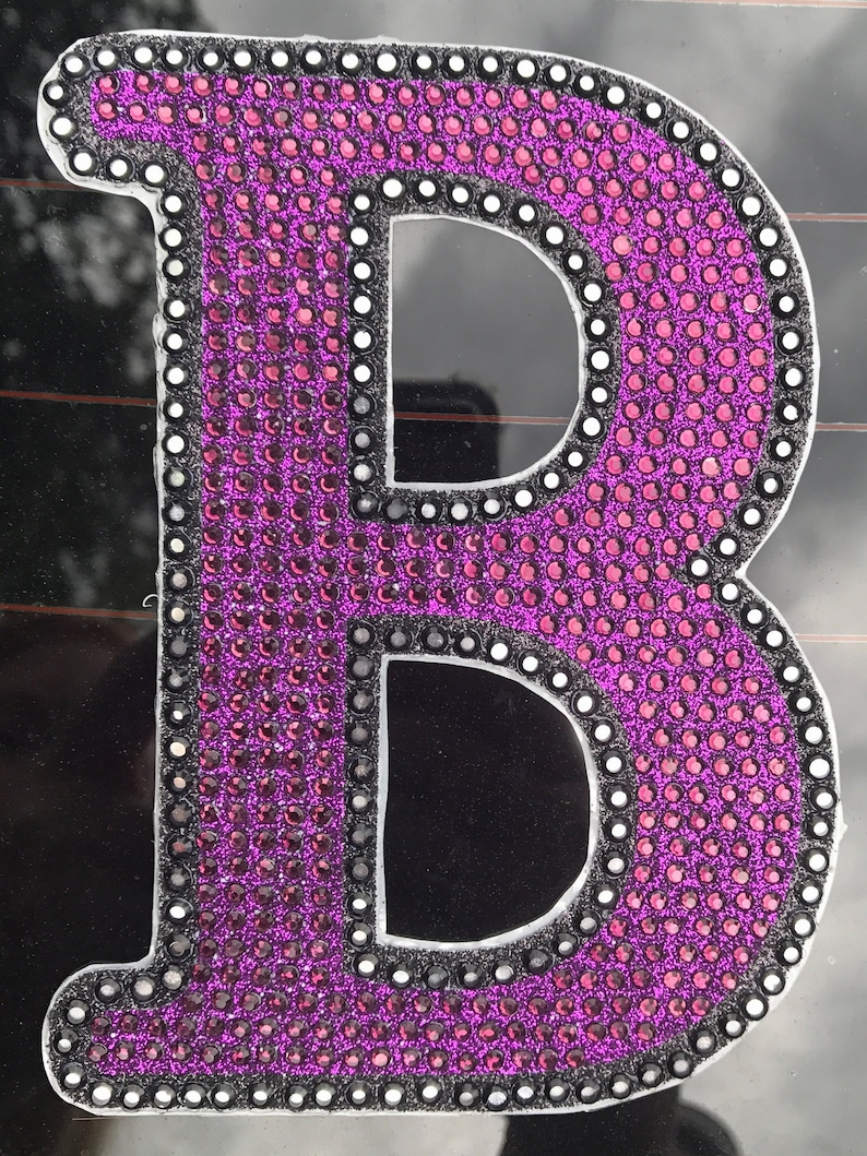 May include: A large, purple letter B made of rhinestones. The letter is outlined in black and has a white border.