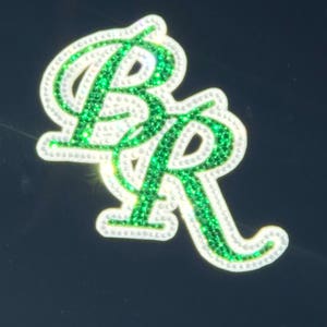 May include: A close-up of a green and white rhinestone sticker with the letters "BR" in a cursive font.