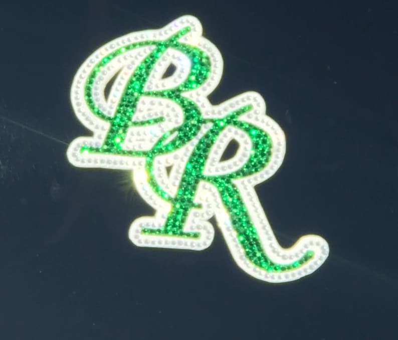 May include: A close-up of a green and white rhinestone sticker with the letters "BR" in a cursive font.