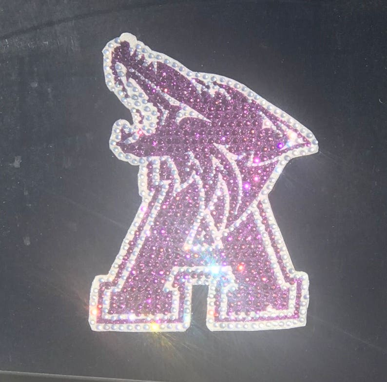May include: A purple and white rhinestone iron-on patch featuring a stylized wolf howling with the letter "A" below it.