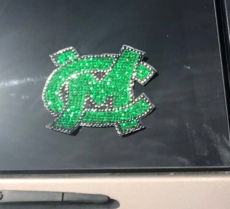 May include: A green and silver car decal featuring the letters "NC" in a stylized font, made of rhinestones.