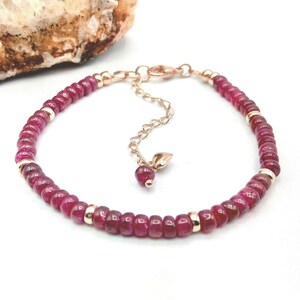 May include: A delicate bracelet featuring small, round, deep red ruby beads and gold accents. The bracelet has a small leaf charm and an adjustable clasp.