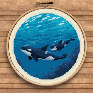Könnte beinhalten: Ein Kreuzstich-Stickrahmen mit einer pixeligen Unterwasserszene mit zwei Orcas. Die Orcas sind schwarz und weiß und schwimmen in blauem Wasser mit Blasen und einem Hauch von Korallen. Der Rahmen ist rund und hat einen Holzrahmen.