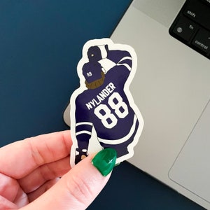 Może przedstawiać: Naklejka z hokeistą w kolorze fioletowym i białym z nazwiskiem "NYLANDER" i numerem "88" z tyłu.