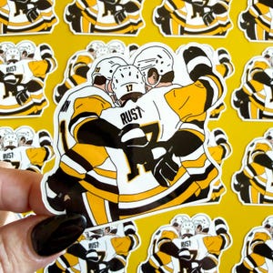 May include: A sticker depicting a hockey team in a celebratory embrace. The players are dressed in black, white, and yellow uniforms. The word "RUST" is printed on the jersey. The background is a repeating pattern of the same sticker.