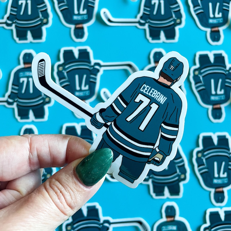 May include: A teal and white hockey player sticker with the name "Celebrini" and the number "71" on the back. The sticker is on a blue background.