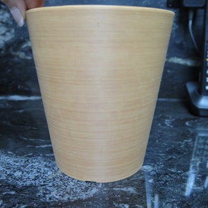 May include: A light brown, cylindrical planter made of a material that resembles wood.