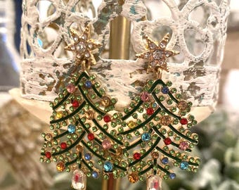 May include: Gold-toned Christmas tree earrings with green enamel branches and colorful gemstone ornaments. Each earring features a star at the top and a rectangular crystal at the bottom. Festive holiday jewelry.