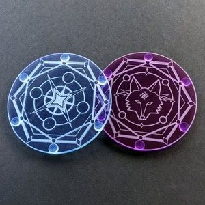 May include: Two round, translucent tokens. One is blue with a star and geometric design. The other is purple with a wolf head and geometric design. Both have a series of small, round accents around the edge. The tokens are on a black surface.
