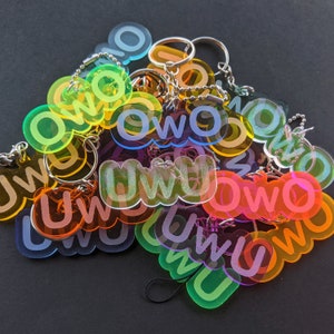 May include: A collection of colorful keychains with the words "owo" and "uwu" printed on them. The keychains are made of clear plastic and have a variety of colors, including pink, blue, green, yellow, and orange.