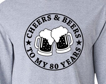 Puede incluir: Camiseta gris de manga larga con un gráfico circular negro que dice "Cheers & Beers to My 80 Years" con dos jarras de cerveza dentro del círculo.