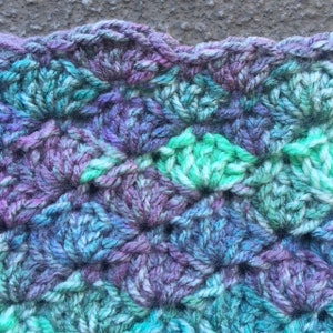 May include: Close-up of a crocheted fabric with a textured pattern in shades of blue, green, and purple.