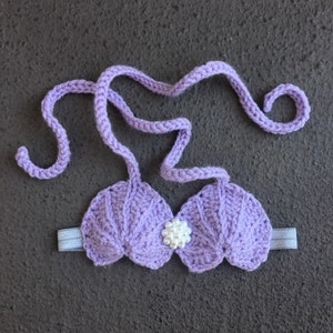 May include: Purple crocheted seashell bra with a white pearl accent. The bra has adjustable straps and a stretchy band.