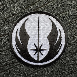 以下が含まれることがあります： ライトセーバーと翼のシンボルが刺繍された白黒のパッチ。シンボルは黒の輪郭のある白い円に囲まれています。