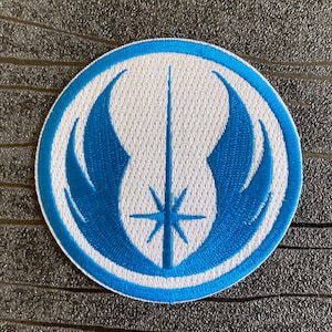 Op de afbeelding: Een blauwe en witte geborduurde patch met het symbool van de Jedi Order. Het symbool is een wit lichtzwaard met een ster aan het einde, omringd door twee blauwe vleugels.