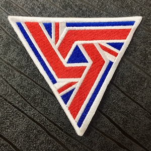 May include: A white, blue and red embroidered patch in the shape of a triangle. The design features a stylised geometric pattern.