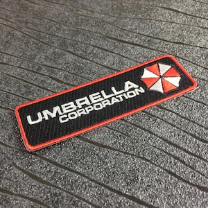 May include: A rectangular black patch with the words "UMBRELLA CORPORATION" in white lettering. The patch has a red border and a logo of a red and white umbrella.