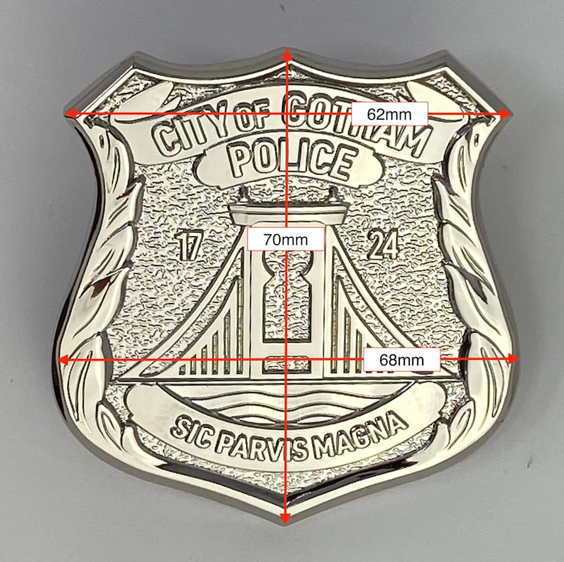 May include: A silver-coloured metal police badge with the text "CITY OF GOTAM POLICE" and "SIC PARVIS MAGNA". The badge features a stylised image of a bridge with the numbers "17" and "24" on either side. The badge measures 62 mm wide and 70 mm tall.