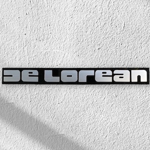 May include: A black and silver rectangular sign with the text "DeLorean" in silver letters.