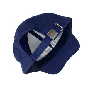 May include: A navy blue baseball cap with a silver metal buckle closure. The cap is turned inside out, showing the white stitching on the inside.