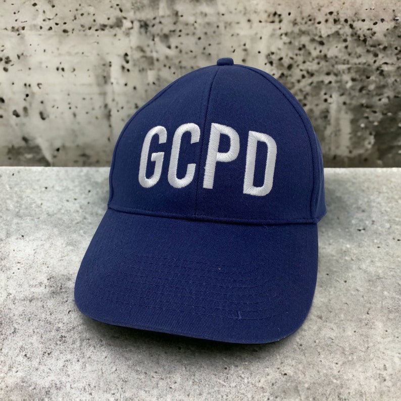 May include: A navy blue baseball cap with white embroidered lettering that reads "GCPD".