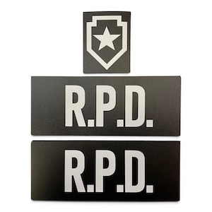 May include: Three rectangular black patches with white lettering and graphics. The top patch features a white star inside a shield outline. The two bottom patches are identical, each displaying the white text R.P.D. in a bold, sans-serif font.