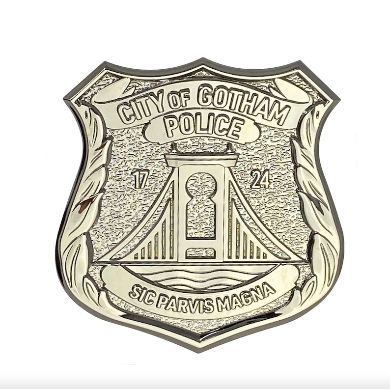 May include: A gold-coloured metal police badge with the words "City of Gotham Police" and "Sic Parvis Magna" inscribed on it. The badge features a stylised bridge with a keyhole in the centre.
