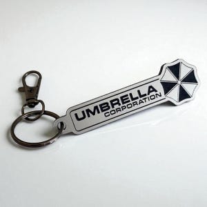 Sleutelhanger met Raccoon City Umbrella Corporation-logo gemaakt van 3 mm aluminium op zwart laminaat acryl.