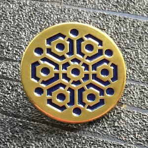 May include: A gold-coloured metal pin with a blue geometric design. The design is a repeating pattern of hexagons and circles.